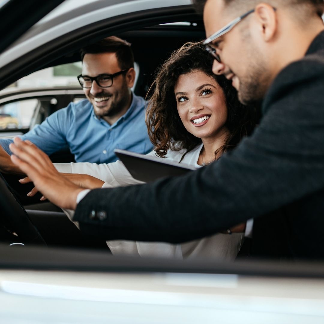 Smiling couple sitting in an electric vehicle as a dealership representative demonstrates features, creating an engaging and trust-building customer experience.